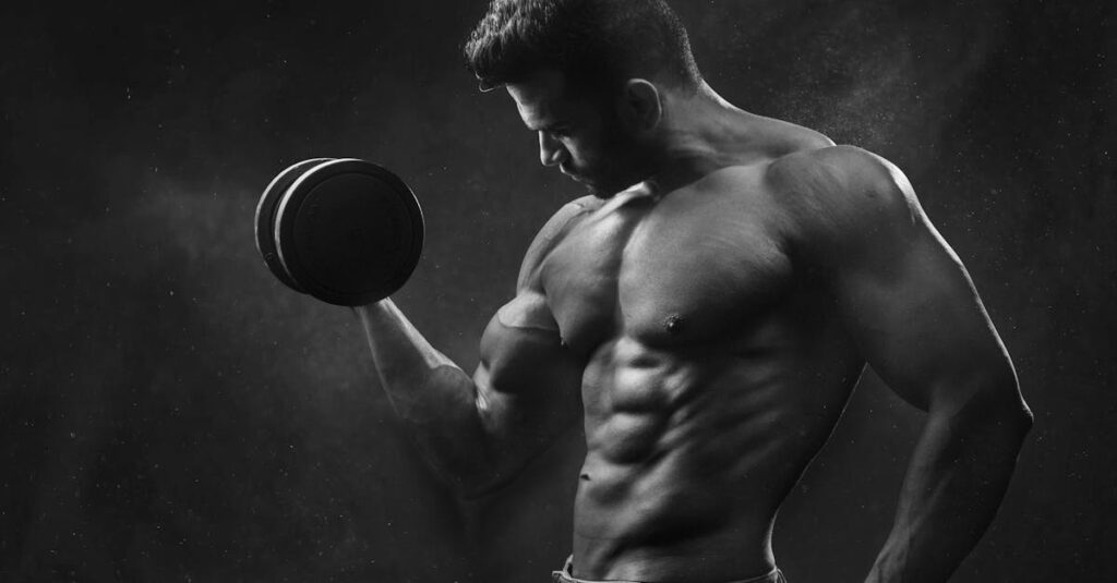 Powerful black and white portrait of a shirtless bodybuilder lifting dumbbells in the gym.