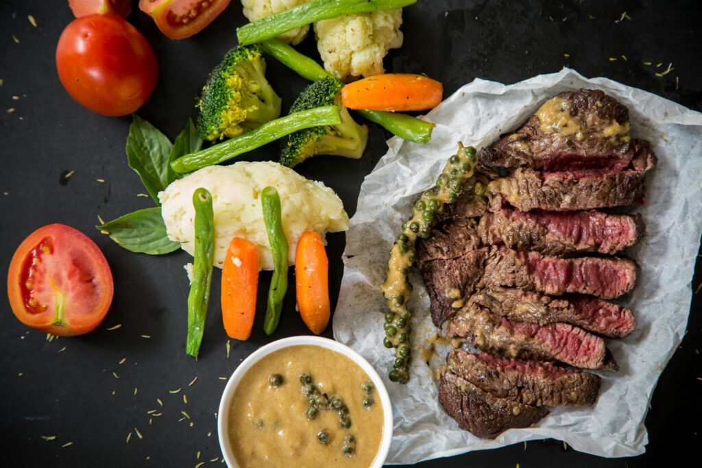 Grilled steak served with fresh vegetables and pepper sauce, presenting a colorful and appetizing meal.