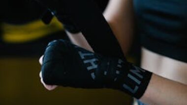 Crop anonymous lady in sportswear using boxing wrap for hand bandaging while training